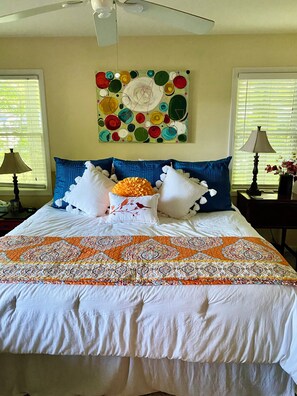 Una cama bien hecha con una colcha estampada, dos almohadas azules y una almohada decorativa con pájaros.