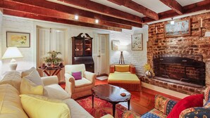 A cozy living room with exposed wooden beams, a fireplace, and a variety of seating options including a sofa, armchairs, and a small table. - Garden Level of Grand Savannah Home (Savannah)