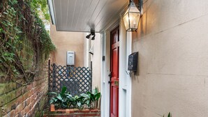 A narrow alleyway with a red door, a brick wall, and a metal fence. - Garden Level of Grand Savannah Home (Savannah)