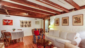A cozy living room with exposed wooden beams, a white brick wall, and a dining area with a striped tablecloth. - Garden Level of Grand Savannah Home (Savannah)