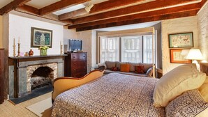 A bedroom with a bed, a dresser, a television, a fireplace, and a window with shutters. - Garden Level of Grand Savannah Home (Savannah)
