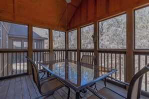 Une terrasse couverte avec une table et des chaises en verre, des rampes en bois et une vue sur un immeuble et des arbres.