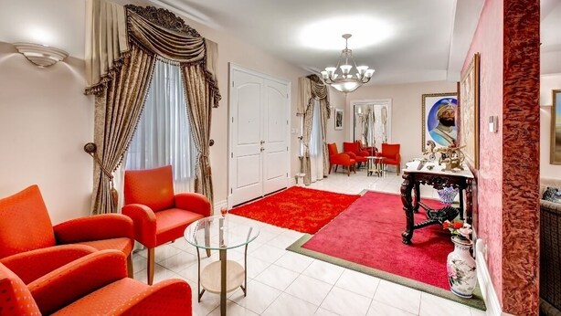 A spacious living room with red chairs, a glass coffee table, and a red rug. There is a dining area with red chairs and a table in the background.