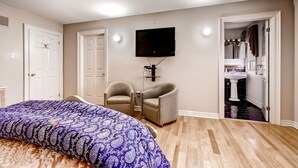 A bedroom with a bed, two armchairs, a TV, and a bathroom visible through an open door.