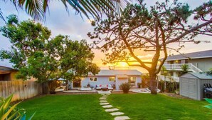Un patio trasero residencial con un césped cuidado, un camino de piedra y un gran árbol que da sombra.
