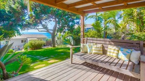 Una terraza de madera con un banco, rodeada de exuberante vegetación y vistas al océano.