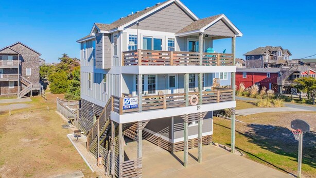 Een twee verdiepingen tellend strandhuis met een balkon, een reddingsboei en een surfplank.