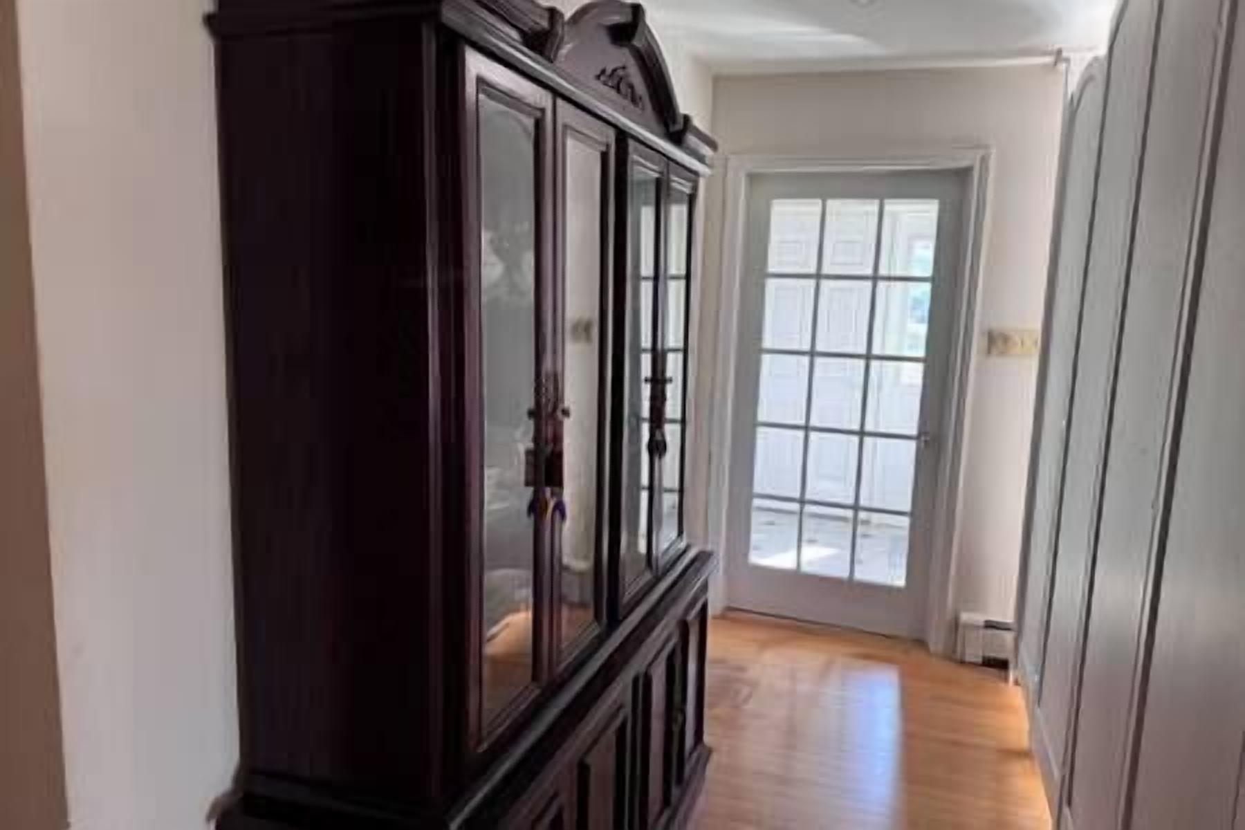 A hallway with a dark wooden cabinet and a door leading to a bright room with a view.
