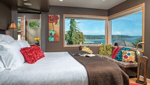A bedroom with a large bed, a view of the outdoors, and a window with a view of a mountain. - Cottage with Puget Sound, Mount Rainier, & Olympic Views (Burien)