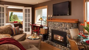 A cozy living room with a stone fireplace, a flat-screen TV mounted above it, and a comfortable seating area with a sofa and armchairs. - Cottage with Puget Sound, Mount Rainier, & Olympic Views (Burien)