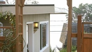 A wooden pergola entrance to a house with a small porch, potted plants, and a window. - Cottage with Puget Sound, Mount Rainier, & Olympic Views (Burien)