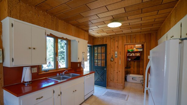 A kitchen with wooden walls, a red countertop, white cabinets, a sink, and a door leading to another room. - Madison River Fishing Cabin (Cameron)