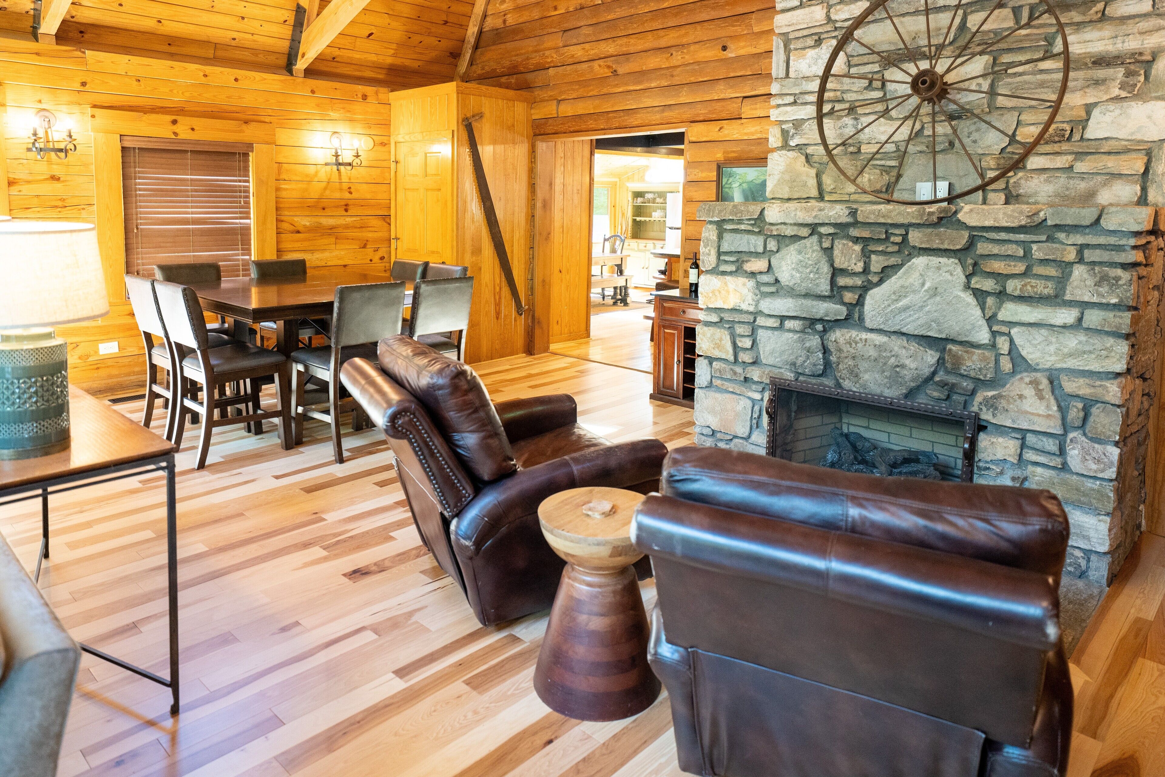 A log cabin interior with leather sofas, a stone fireplace, wooden flooring, and a dining area.