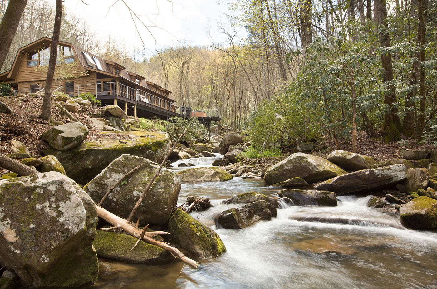 Una cabaña rústica con fachada de madera, un balcón y vistas a un arroyo con rocas.