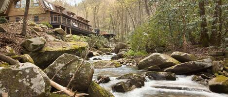 Una cabaña rústica con fachada de madera, un balcón y vistas a un arroyo con rocas.