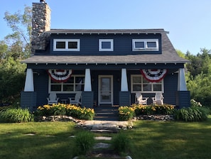 Enjoy the charm of this two-story house with a front porch featuring Adirondack chairs and a small table.