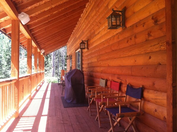 A wooden cabin with a covered porch, wooden chairs, a barbecue grill, and a lantern.