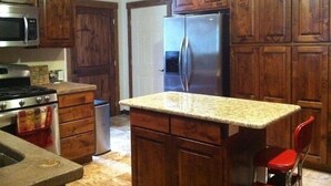 A kitchen with wooden cabinets, a stainless steel refrigerator, a microwave, a stove, and a red chair. - King's Cabin, just 2 miles from the Park entrance in West Glacier! (West Glacier)