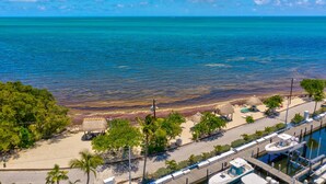 Blick auf die Küste mit Strand, strohgedeckten Gebäuden und einem Hafen mit Booten.