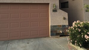 Un edificio residenziale con garage, una finestra con persiane, un piccolo portico e un cespuglio di fiori.