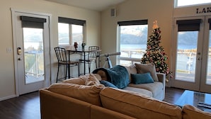 A cozy living room with a large window, a Christmas tree, and a dining area with chairs and a table. - Expansive views, hot tub, & kid friendly! Perfect for multiple families! (Manson)