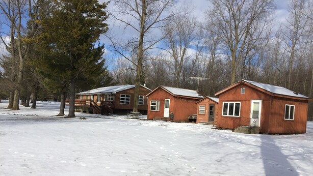 A row of wooden cabins with a snow-covered ground, surrounded by trees. - Schuster's Fox River Resort on the Fox -Perch Place (Omro)