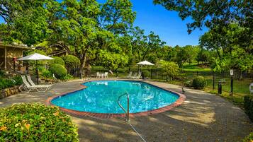 A circular pool with a surrounding deck, lounge chairs, and umbrellas.