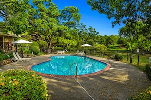 A circular pool with a surrounding deck, lounge chairs, and umbrellas.