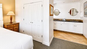 Ein Hotelzimmer mit einem Bett, einem Nachttisch mit Lampe, einem Kleiderschrank und einem Badezimmer mit Waschbecken, Spiegel und Fliesenboden.
