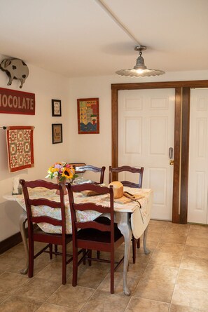 A dining area with a table set for four, wooden chairs, a chandelier, and a door in the background.