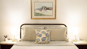 Una cama bien hecha con ropa de cama cuadriculada, un cojín floral y un cuadro enmarcado encima.