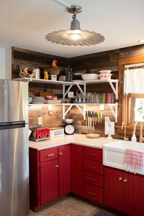 A kitchen with a stainless steel refrigerator, a red cabinet, a white sink, and a hanging knife rack.