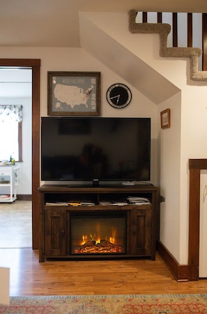 A living room with a flat-screen TV, a fireplace, a framed map, and a clock on the wall.