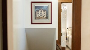 A hallway with a staircase leading to a bedroom. There are framed pictures on the wall.