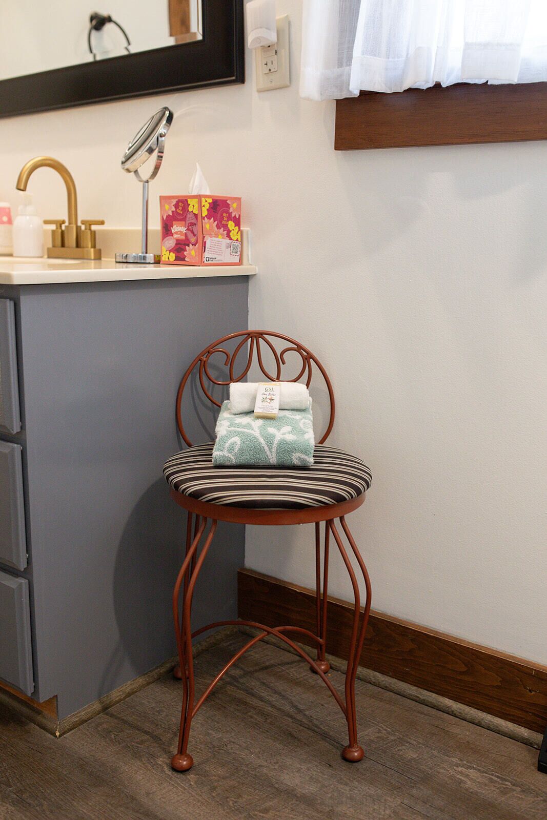 A bathroom with a wooden-framed chair, a sink with a faucet, and a mirror above the mirror.
