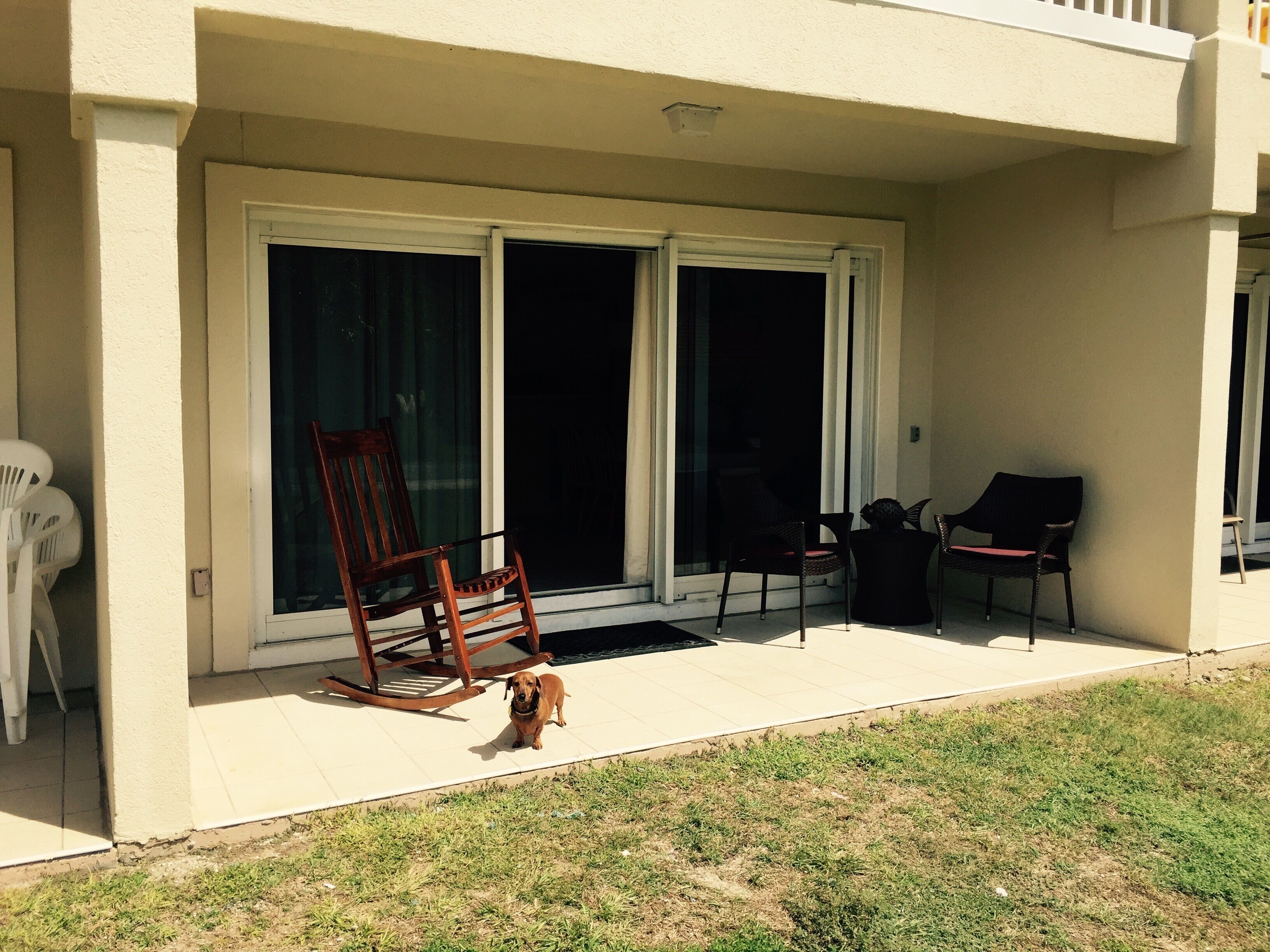 A covered patio area with a sliding glass door, a wooden rocking chair, and two lounge chairs.