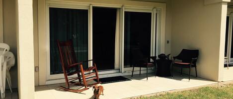 A covered patio area with a sliding glass door, a wooden rocking chair, and two lounge chairs.