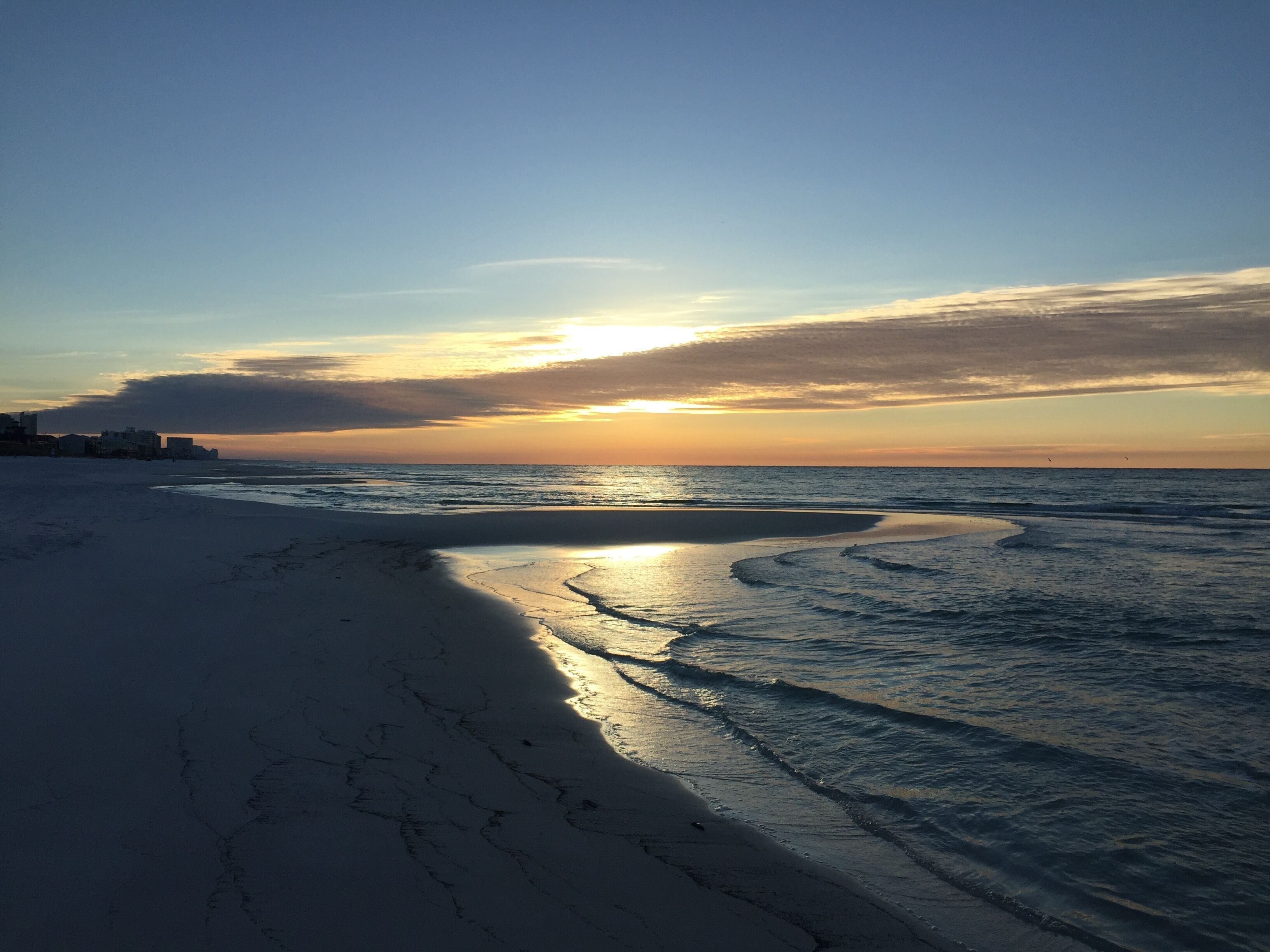 Een strand met een heldere lucht en de zon die in de oceaan ondergaat.