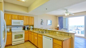A kitchen with wooden cabinets, a microwave, an oven, a dishwasher, and a large island with a sink. - Ariel Dunes I 2205 - Absolutely Breathtaking Scenery From Your Balcony! (Miramar Beach)