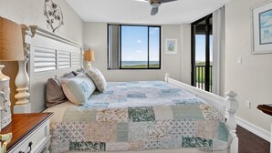 Een slaapkamer met een groot bed, een plafondventilator, een raam met uitzicht en een open haard.