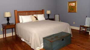 Un dormitorio con una cama de madera, dos mesitas de noche con lámparas, un aparador azul y un cuadro en la pared.