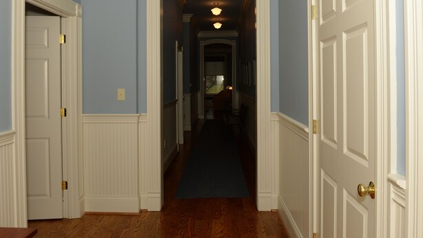 Un pasillo con piso de madera, puertas blancas y una alfombra azul que conduce a una habitación con ventana.
