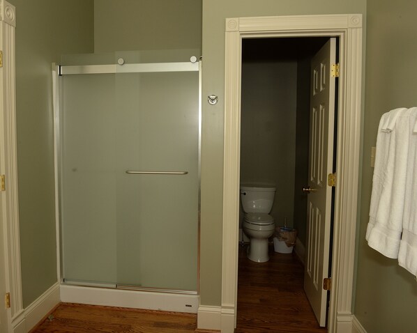 A bathroom with a glass-enclosed shower, a toilet, and a towel hanging on the wall. - Renovated train station on thoroughbred horse farm. (Paris)