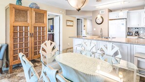 Una cocina moderna con armarios blancos, encimera de granito y comedor con mesa y sillas de vidrio.