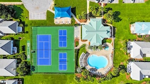 An aerial view of a residential area with a large tennis court, a swimming pool, and several houses.