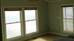 Un dormitorio con cama, ventanas amplias, ventilador de techo y vista al agua.