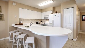 A kitchen with white cabinets, a large island with stools, a microwave, and a refrigerator.