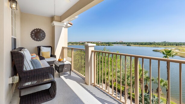 A balcony with wicker furniture, a ceiling fan, and a view of a lake. - Top Floor 2000 sq ft Lakefront Corner Condo | Walk to Epic (Orlando)