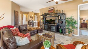 A spacious living room with a leather sofa, a coffee table, and a television. There is a ceiling fan, a fireplace, and a dining area in the background. - Top Floor 2000 sq ft Lakefront Corner Condo | Walk to Epic (Orlando)