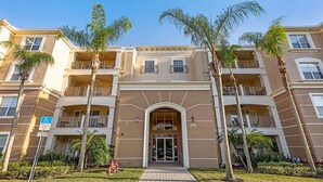 A multi-story hotel with a central entrance, balconies, and palm trees. - Top Floor 2000 sq ft Lakefront Corner Condo | Walk to Epic (Orlando)
